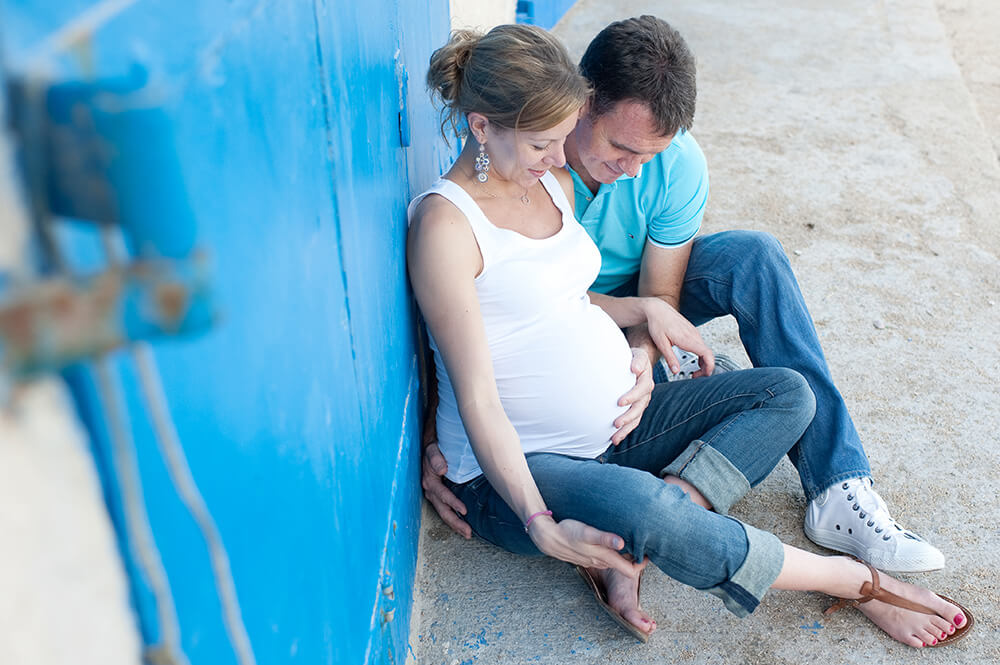 Homme tenant le ventre de sa femme enceinte. Tous les deux assis par terre.