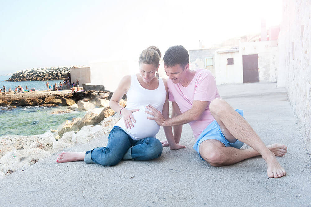 Couple assis par terre avec les mains sur le ventre tout rond de la femme enceinte