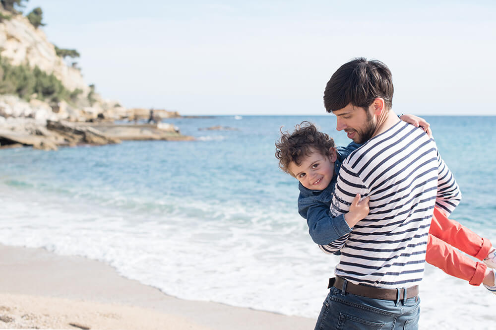 Môme dans les bras de son père jouant sur la plage.