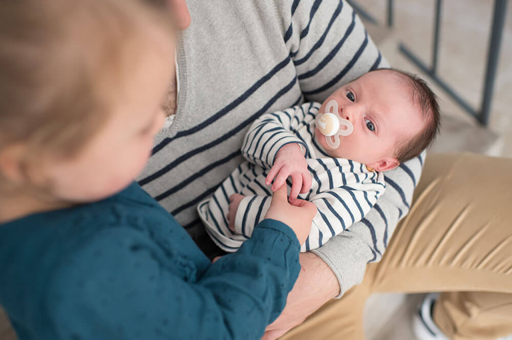 Grande sœur qui prend la main de son petit frère. Photo fratrie à la maison.