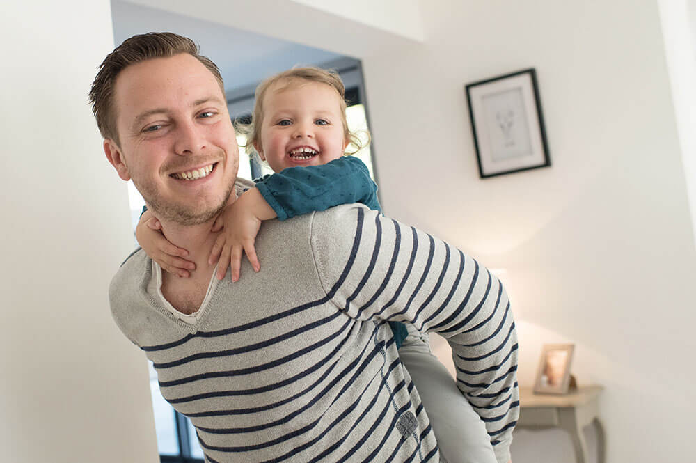 Enfant avec un grand sourire jouant sur le dos de son papa.