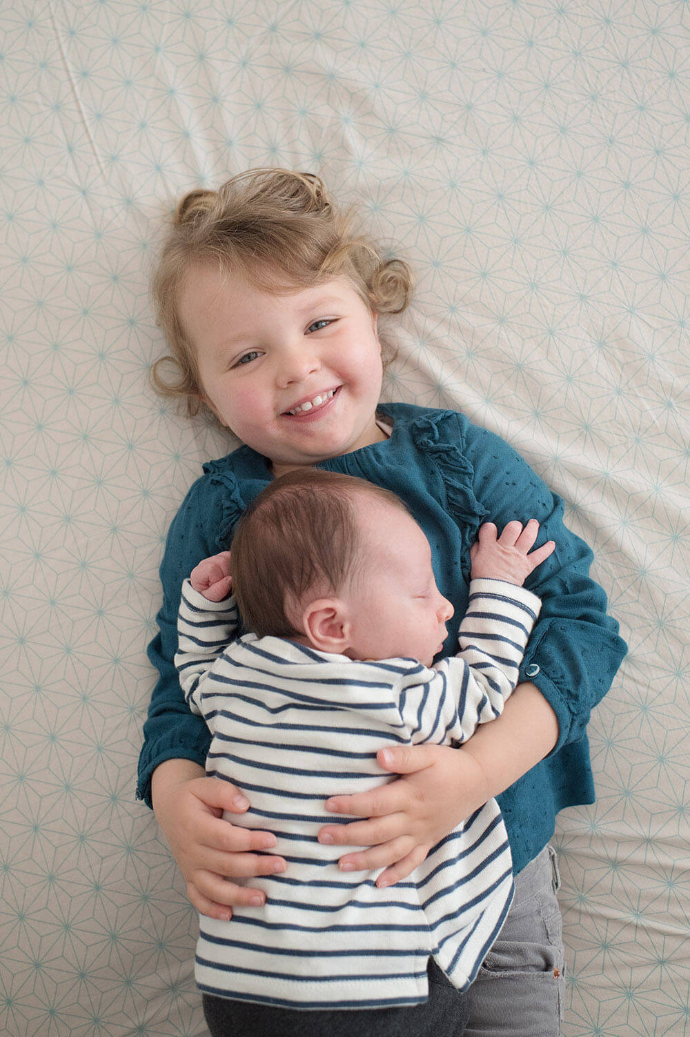 La grande sœur qui porte son petit frère sur le lit.