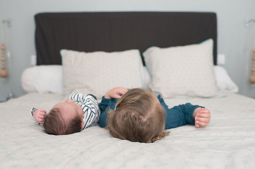 Petit frère et grande sœur allongés sur le lit des parents