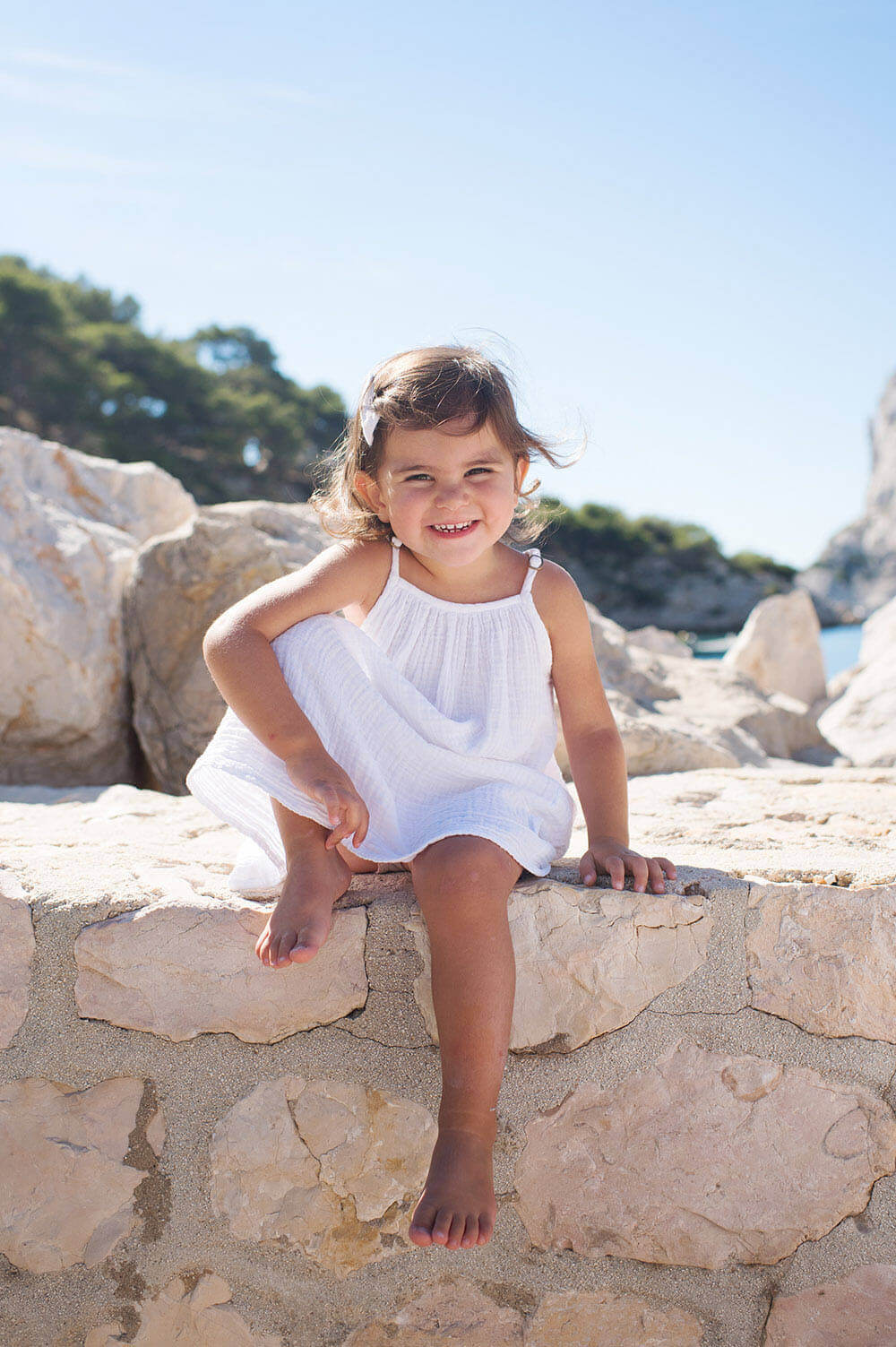 Portrait d'enfant pied nu assise sur un muret avec un grand sourire