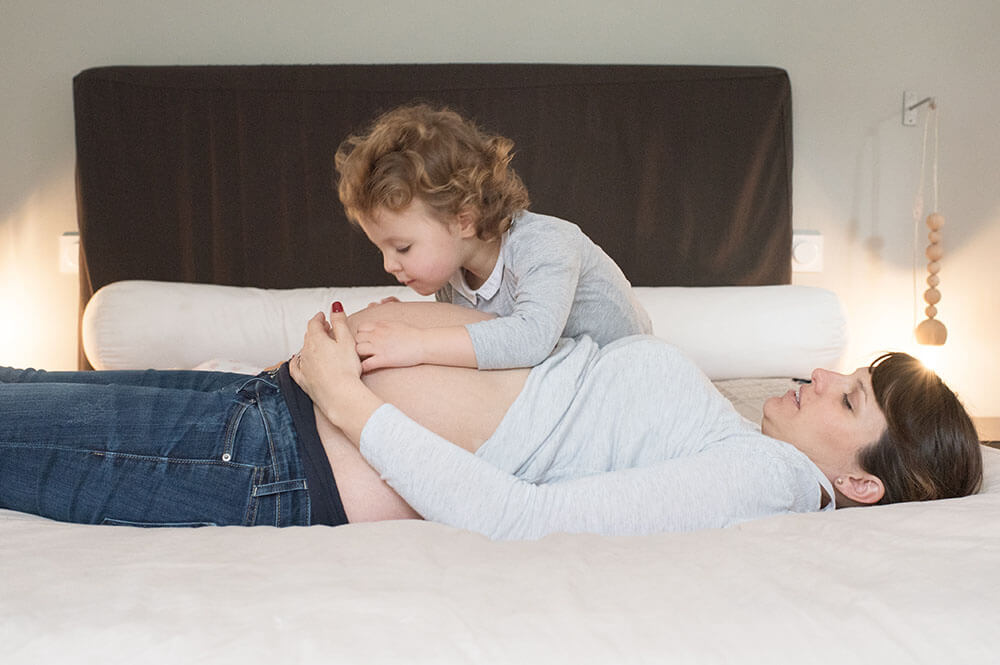 Grande sœur faisant un bisous sur le ventre de sa maman.