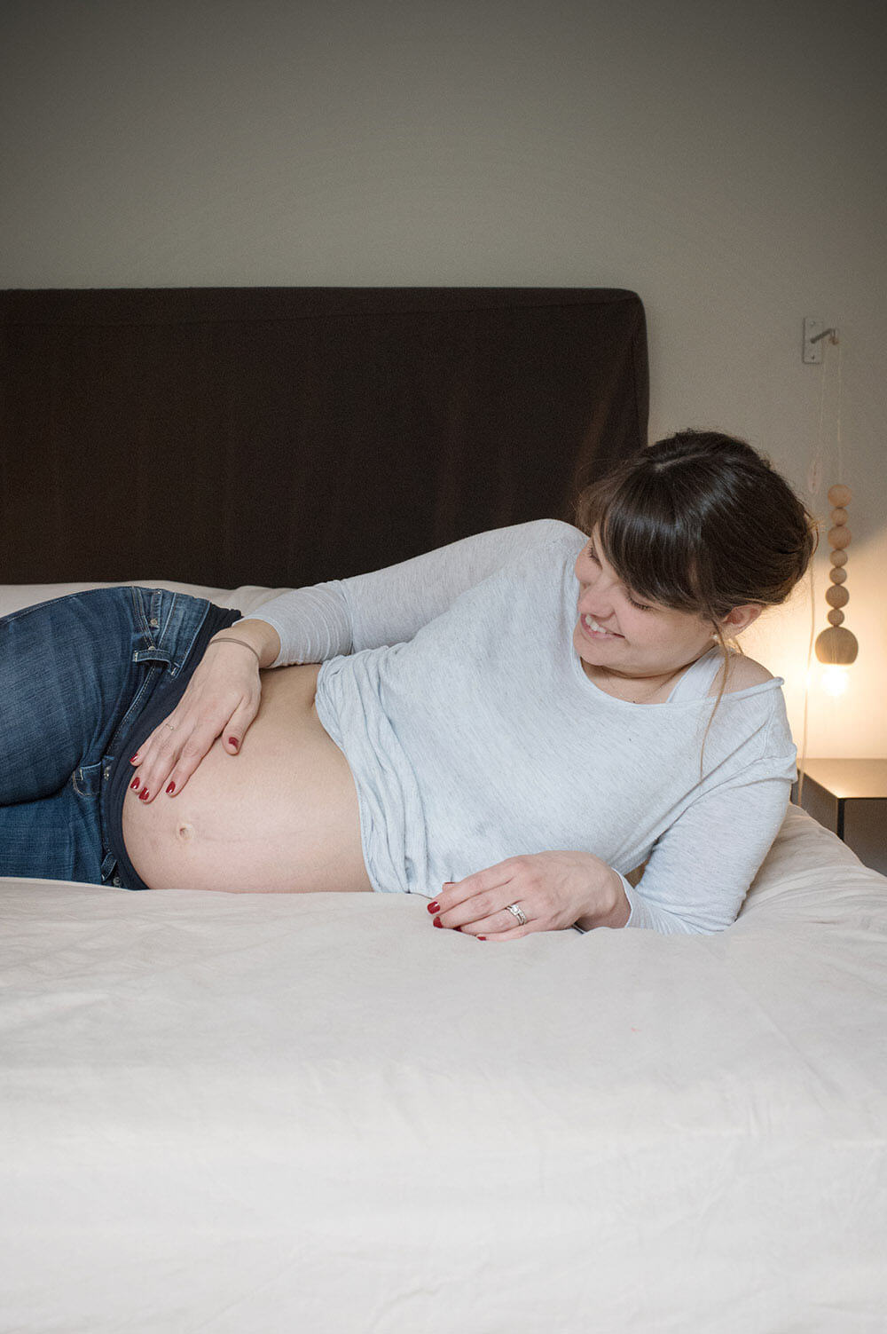 Femme enceinte plongée sur son lit se touchant le ventre.