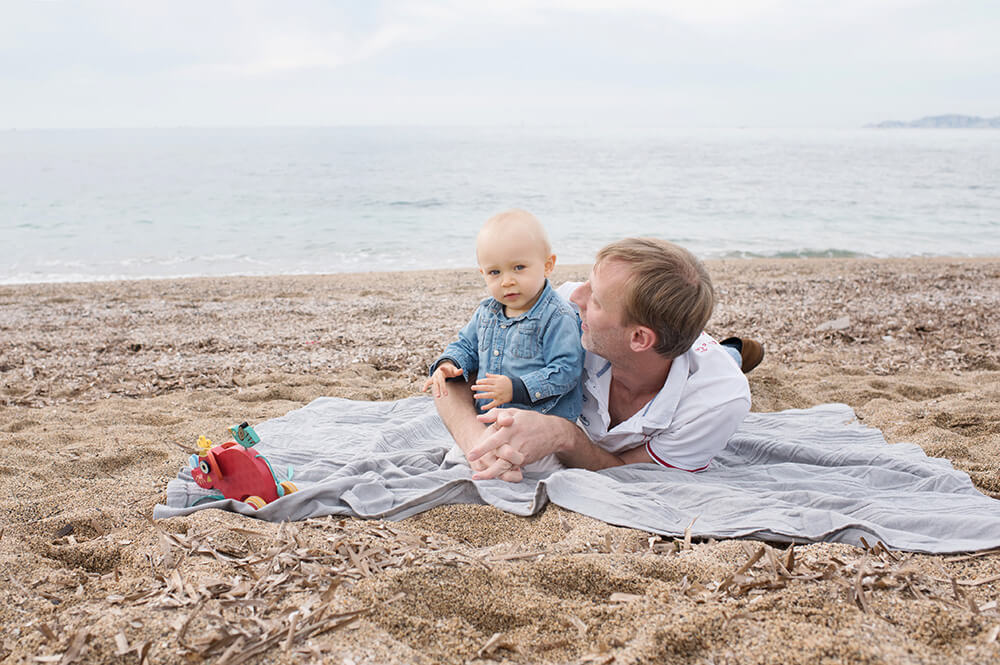Bambin et son papa allongés sur une couverture sur le sable.