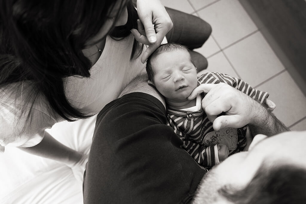 Nouveau-né se faisant câliner par ses parents. Photo originale en NB.