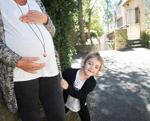 Enfant se cachant derrière le gros ventre de sa maman enceinte.