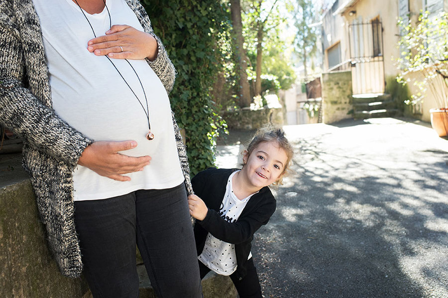 Enfant se cachant derrière le gros ventre de sa maman enceinte.