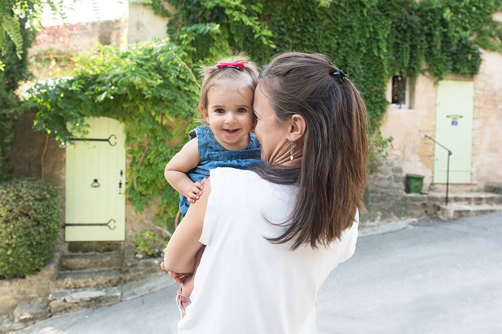 Portrait enfant dans les bras de sa mère devant une jolie façade de maison.