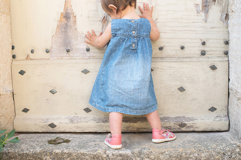 Enfant de un an se tenant debout devant une porte ancienne.