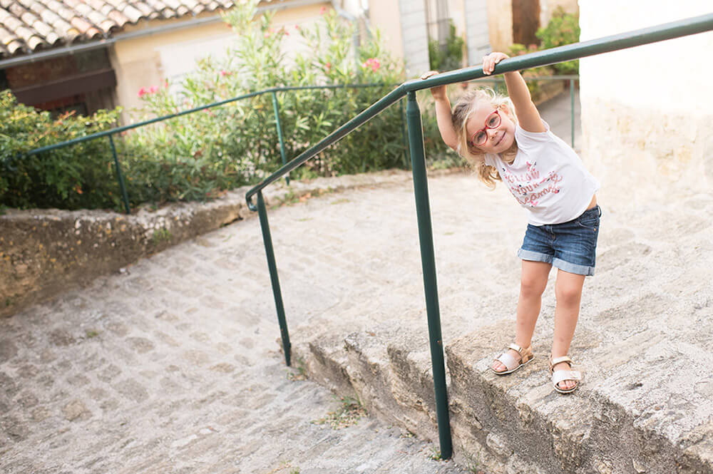 Portrait d'enfant à Ansouis Jouant avec une rambarde verte.