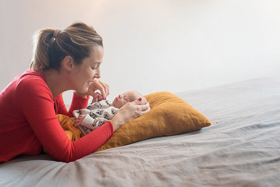 Nouveau-né allongé sur un coussin moutarde et sa maman lui tenait sa petite main.