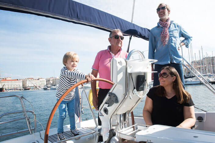 Portfolio famille Marseille. Enfant tenant la barre du voilier.